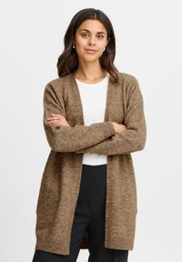 Cardigan lungo marrone realizzato in un morbido tessuto testurizzato, con davanti aperto e polsini a costine. Indossato sopra una maglietta bianca, ha una vestibilità comoda.