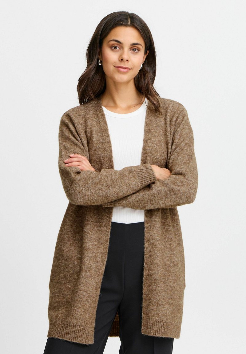 Cardigan lungo marrone realizzato in un morbido tessuto testurizzato, con davanti aperto e polsini a costine. Indossato sopra una maglietta bianca, ha una vestibilità comoda.