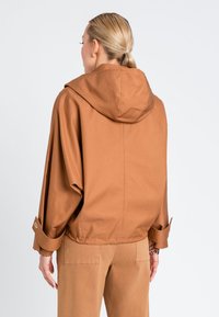 Giacca con cappuccio marrone di taglio rilassato, con maniche ampie e orli arrotolati. Tessuto morbido, design senza fronzoli e tessuto leggero.