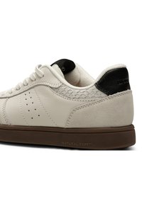 Bijele kožne tenisice sa akcentima od suede-a, teksturiranim crnim petom, smešnim gumiranim đonom i perforiranim detaljima sa strane. Prikaz brenda Natural Soft.