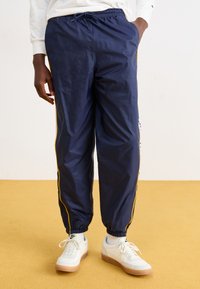 Joggers in rete blu navy con strisce gialle ai lati, vita elastica e polsini. Abbinati a sneakers bianche con suola in gomma.