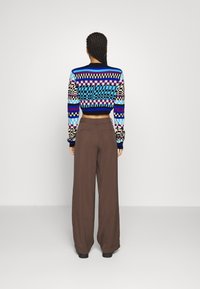 Kolorowy krótki sweter z geometrycznymi wzorami; w zestawieniu z brązowymi, szerokimi spodniami. Sweter charakteryzuje się dzianą fakturą i żywymi kolorami.