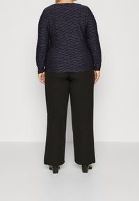 Marinblå långärmad topp med ett strukturerat vågmönster och svarta avslappnade byxor. Båda plaggen är tillverkade av mjuka material med eleganta detaljer.