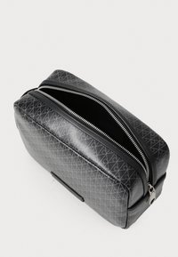 Zwarte tas met geometrisch patroon, een gladde textuur, ritssluiting en zilveren hardware accenten. Rechthoekige vorm met een gestructureerd ontwerp.