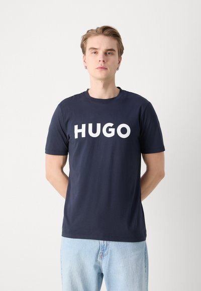 тъмносин памучен tshirt с голям бял текст "HUGO" отпред, кръгло деколте и къси ръкави. Свободен стил с меко усещане.