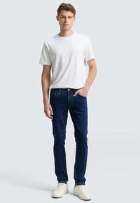 Biała koszulka z krótkim rękawem zestawiona z ciemnoniebieskimi dżinsami i białymi trampkami. Jeansy mają pięć kieszeni oraz zapięcie na guziki.