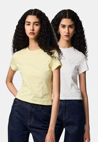 Dos camisetas crop top exhibidas: una es amarilla clara y la otra blanca, ambas de manga corta. Se combinan con vaqueros de mezclilla oscura.
