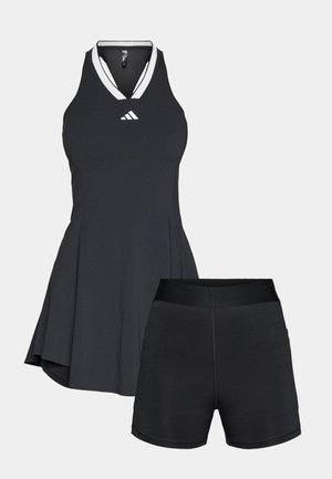 Schwarzes sportliches Kleid mit tailliertem Oberteil, V-Ausschnitt und ausgestelltem Rock; kombiniert mit schwarzen Shorts mit breitem elastischem Bund.