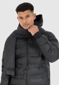 Schwarze Steppjacke mit markentypischer Textur und Reißverschluss. Kombiniert mit einem dunkelgrauen gestrickten Schal. Glattes Material und praktische Gestaltung.