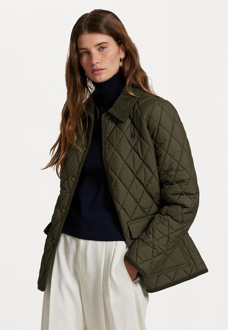 Quilted olive green jacket with a corduroy collar, front snap closure, and side pockets. Worn over a navy turtleneck.