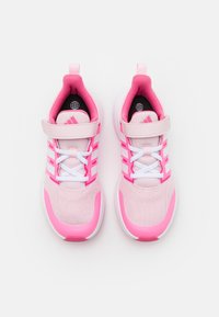 Scarpe da ginnastica rosa con tomaia in rete, dettagli bianchi, cinturino in Velcro e lacci bianchi. Punta arrotondata e suola bianca imbottita.