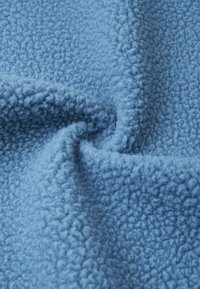Tissu en polaire bleu doux avec une surface texturée et duveteuse, présentant une apparence légèrement froissée qui met en valeur sa chaleur et son confort.