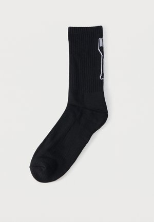 Chaussette noire côtelée mi-mollet avec un motif blanc en forme de fourche verticale sur le côté, présentée sur un fond blanc uni.