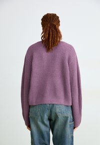 Suéter de punto morado con textura acanalada, diseño corto y hombros caídos, combinado con pantalones de mezclilla azules que cuentan con bolsillos traseros.