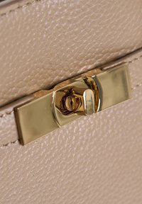 Primo piano di una chiusura a scatto in metallo dorato su pelle textured beige, che tiene chiuso il lembo di una borsa o una pochette.
