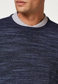 Maglione blu scuro con un motivo a maglia testurizzato, caratterizzato da un colletto polo grigio a contrasto e bordi blu navy attorno al collo.