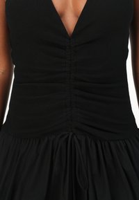 Μαύρο φόρεμα με βαθύ V-ντεκολτέ και οριζόντιες ραφές στο μπούστο. Η φούστα είναι ρέουσα και συγκεντρωμένη με ρυθμιζόμενες ζώνες στη μέση.