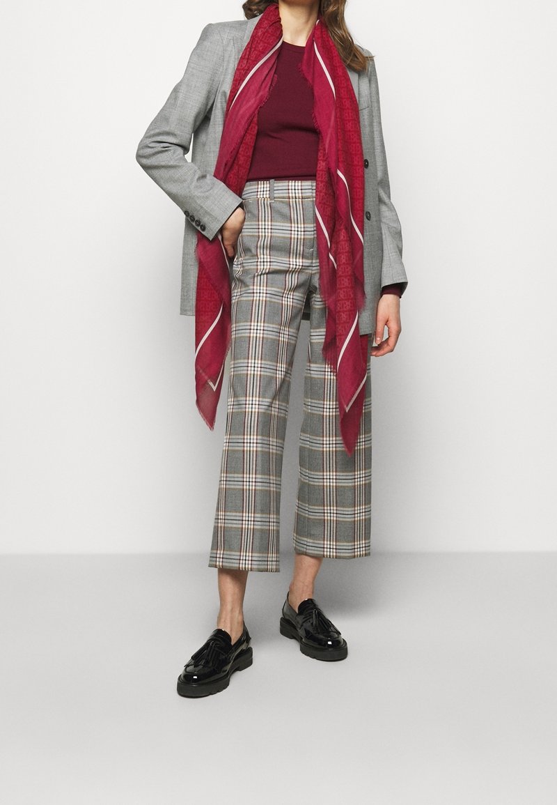 Grå blazer över en vinröd topp, rutig cropped byxor i grått och beige, lager på lager med en burgundysk scarf. Svarta lackskor med snörning fulländar looken.