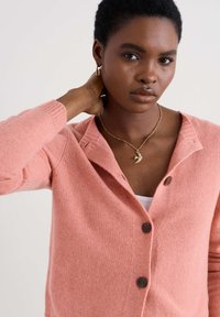 Világos rózsaszín kardigán, kellemes tapintású anyagból, sálgallérral, gombos zárással és bordázott mandzsettákkal. Barna gombokkal díszítve.