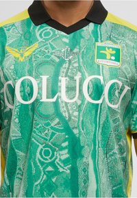 Grüne und gelbe gemusterte Sporttrikot mit schwarzem Kragen, "COLUCCI"-Text und dem Logo des Fußballvereins Kitzbühel auf der Brust.