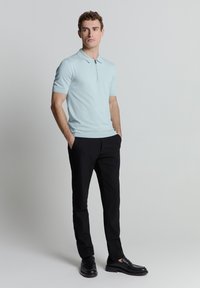 Lichtblauwe poloshirt met korte mouwen en een ritssluiting, gecombineerd met zwarte broek en zwarte instappers. Soepele textuur en aansluitend ontwerp.