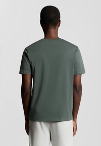 Groene T-shirt met korte mouwen gemaakt van zacht katoen, met een ronde hals en een gladde textuur, gezien vanaf de achterkant.