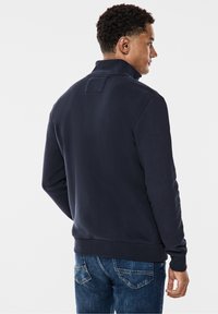 Sudadera azul marino con cuello alto, textura suave, puños y dobladillo de canalé; combinada con jeans de mezclilla azules. Diseño liso sin patrones visibles.