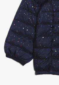 Marineblå pufferjakkeærme med quiltet design, prydet med flerfarvede firkantede pailetter og elastiske manchetter for en sikker pasform.