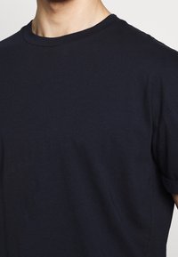 Tmavě modré bavlněné tričko s kulatým výstřihem a krátkými rukávy, s hladkou texturou a minimalistickým designem.
