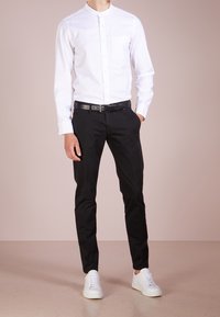 Camicia bianca a collo alto con bottoni, pantaloni neri, cintura nera e sneaker bianche. Design minimalista, forma aderente, texture liscia. Nessun motivo.