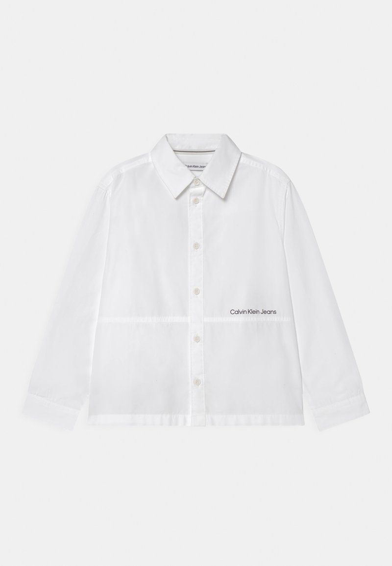 Biała koszula zapinana na guziki, wykonana z gładkiego materiału, z kołnierzykiem rozłożystym, długimi rękawami i małym logotypem "Calvin Klein Jeans" na dole.