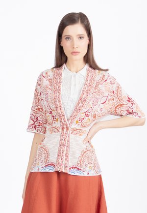 Mujer con camisa blanca de encaje con cuello y cárdigan estampado en tonos rosa y naranja con mangas hasta el codo, combinados con una falda color óxido.