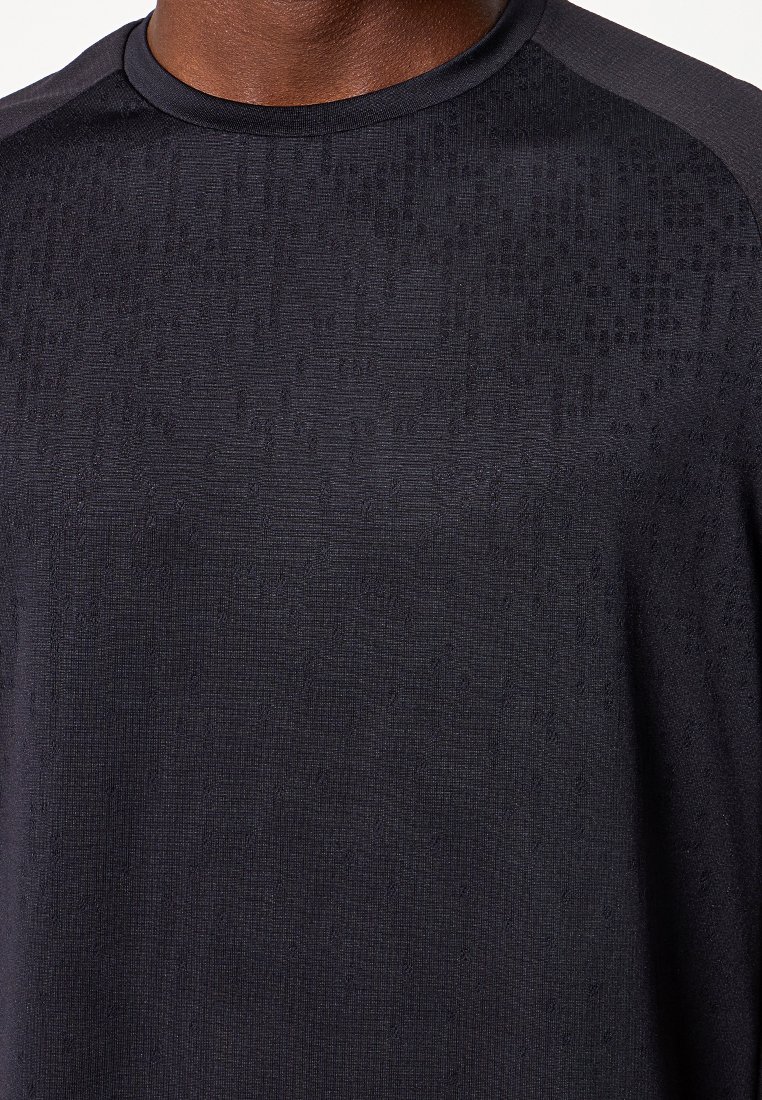 Czarny sportowy T-shirt z teksturowanej tkaniny, krótkimi rękawami raglanowymi i subtelnym wzorem. Miękki materiał o właściwościach odprowadzających wilgoć.