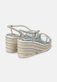 Sandalias de cuña con correas plateadas y suela de yute trenzado. Presentan una plantilla metálica, correas texturizadas y un diseño que realza la altura.
