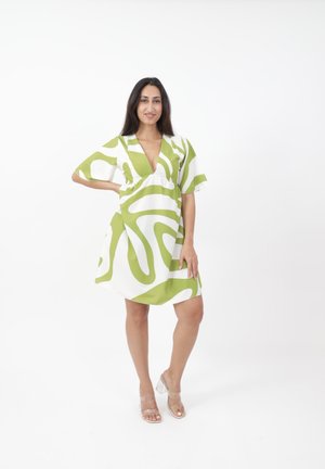 Kleid mit kurzen Ärmeln in einem weißen und grünen abstrakten Muster, mit einem tiefen V-Ausschnitt und lockerer Passform. Transparente Sandalen mit Absatz runden den Look ab.