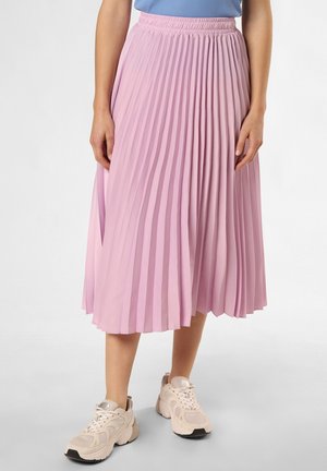 Woman wearing a light purple pleated midi skirt paired with cream chunky sneakers and a blue top, standing on a gray floor.