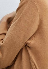 Suéter marrón de punto que presenta un primer plano de una textura suave y puños ajustados, con costuras visibles a lo largo de las mangas.