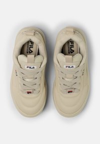 Sneaker beige con una toma in materiale sintetico liscio, lacci testurizzati e colletto imbottito. Presenta un logo sulla linguetta e sottili accenti di colore.