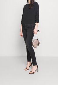 Černá mikina, černé džíny a černé lodičky na jehlovém podpatku. Doplněno texturovanou šedou kabelkou s řetízkovým popruhem a páskem s logem.