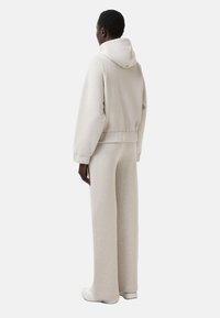 Lys grå hættetrøje og brede bukser, lavet af blødt stof. Har hætte, afslappet pasform og ribbestrikkede manchetter. Minimalistisk design uden mønstre.