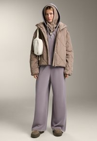 Prošívaná béžová bunda s kapucí, přes kterou je navlečená levandulová mikina a ladící široké kalhoty. Texturovaný šátek jako doplněk a kabelka z umělé kožešiny.