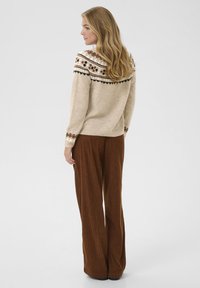 Pull en maille beige avec un empiècement à motifs, présentant des accents marron et noir ; associé à un pantalon en velours côtelé marron à jambes larges.
