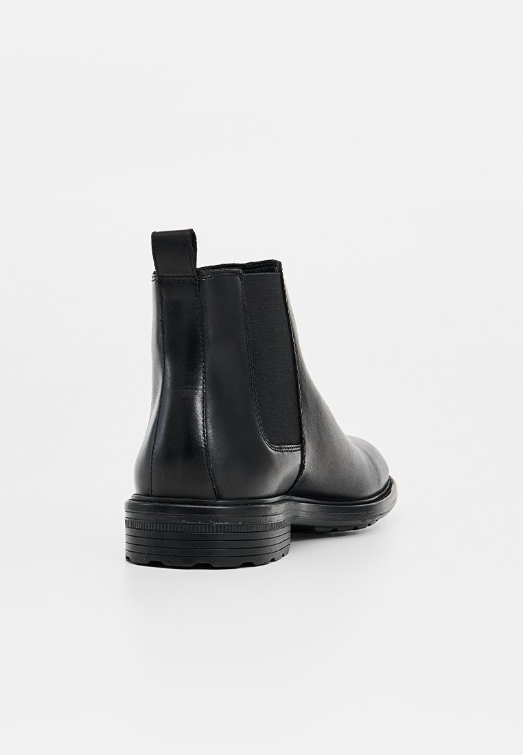 Botas Chelsea negras de cuero con paneles laterales elásticos, punta redonda y suela de goma texturizada para mayor agarre. Acabado suave y lengüeta en la parte posterior.