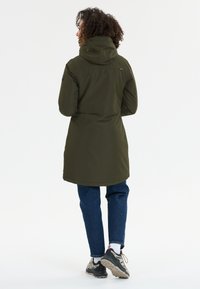 Olivgrön, knälång jacka med huva, med dragkedjestängning och en något smalare passform, bärs över mörkblå jeans och sneakers.