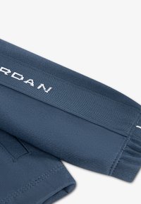 Κοντινό πλάνο διπλωμένου ύφασματος σκούρου μπλε με λευκά ραμμένα γράμματα «JORDAN» σε ελαστική ριγέ μέση ή μανσέτα.