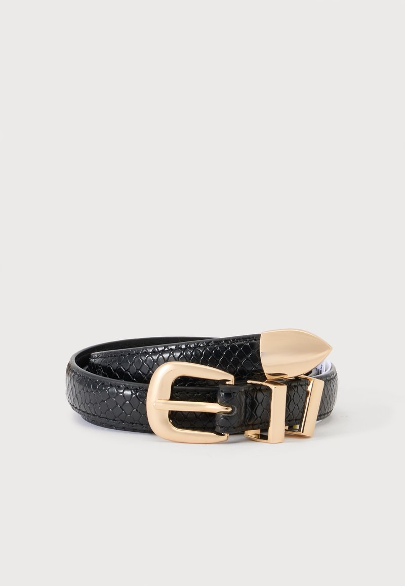 Ceinture en cuir noir texturé avec boucle et pointe dorées, enroulée sur un fond gris clair uni.