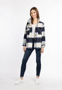Karierte Jacke in Marineblau und Creme mit Kragen, Knopfverschluss und zwei Brusttaschen. Kombiniert mit dunkelblauen Jeans und weißen Turnschuhen.