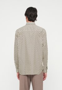 Lange mouw shirt in crème met een geometrisch zwart patroon, klassieke kraag, knoopsluiting en afgeronde zoom, weergegeven vanuit de achterkant.