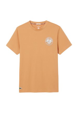 Camiseta de manga corta color marrón claro con el logo de Roland Garros París en el pecho y el logo del cocodrilo de Lacoste en el dobladillo inferior izquierdo.