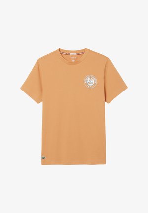 Camiseta de manga corta color marrón claro con el logo de Roland Garros París en el pecho y el logo del cocodrilo de Lacoste en el dobladillo inferior izquierdo.
